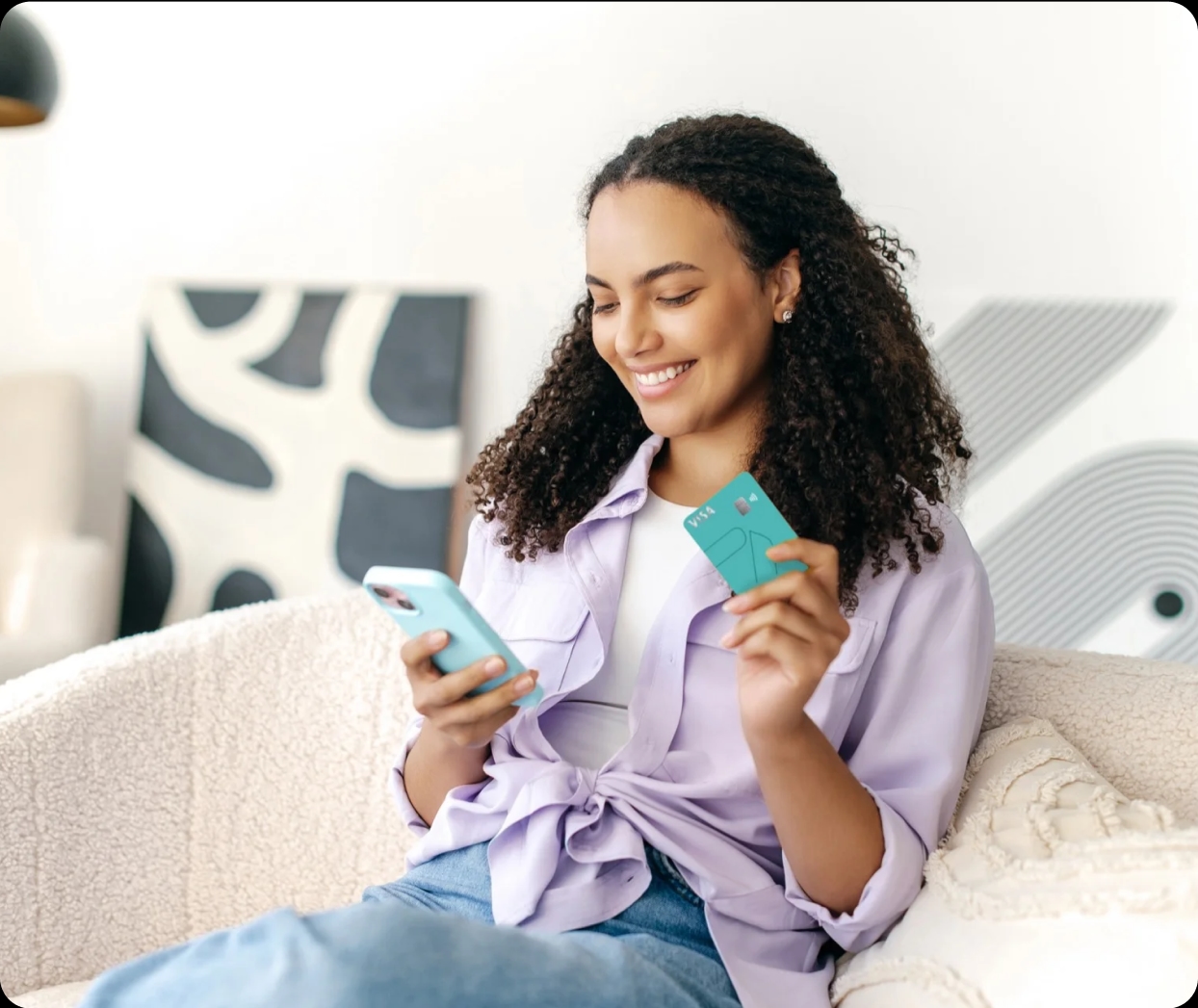 Na imagem você vê uma jovem negra com um belo cabelo cacheado e um belo sorriso enquanto segura o METTAcard em uma mão e acessa o aplicativo com a outra utilizando o celular